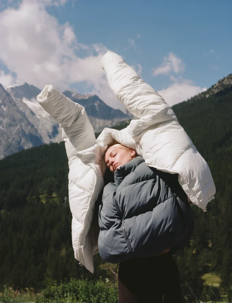 Woman modeling Ernest Leoty winter puffer jackets in a mountainous landscape, highlighting movement and style.