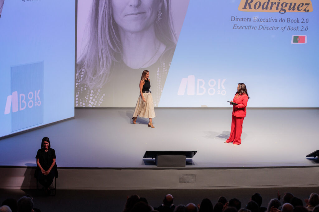 Silvia Pazos Rodriguez on stage at Book 2.0 with her name on the screen behind her