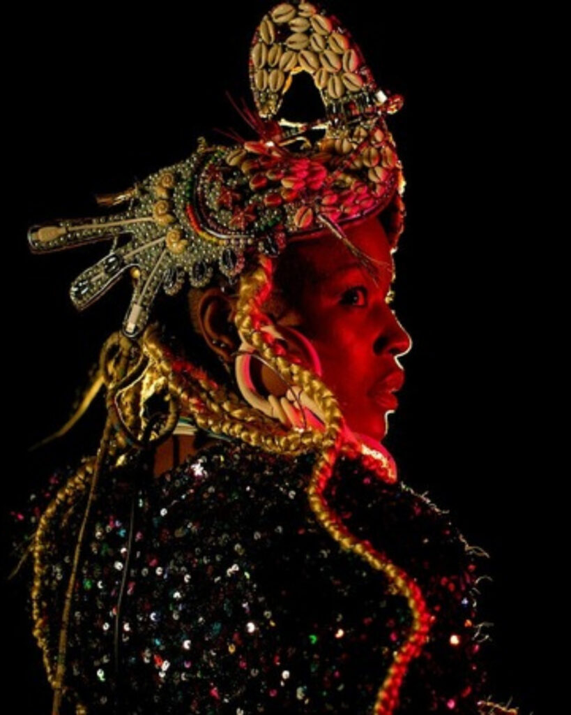 Performer in a golden headdress lit in red, Alkantara Festival