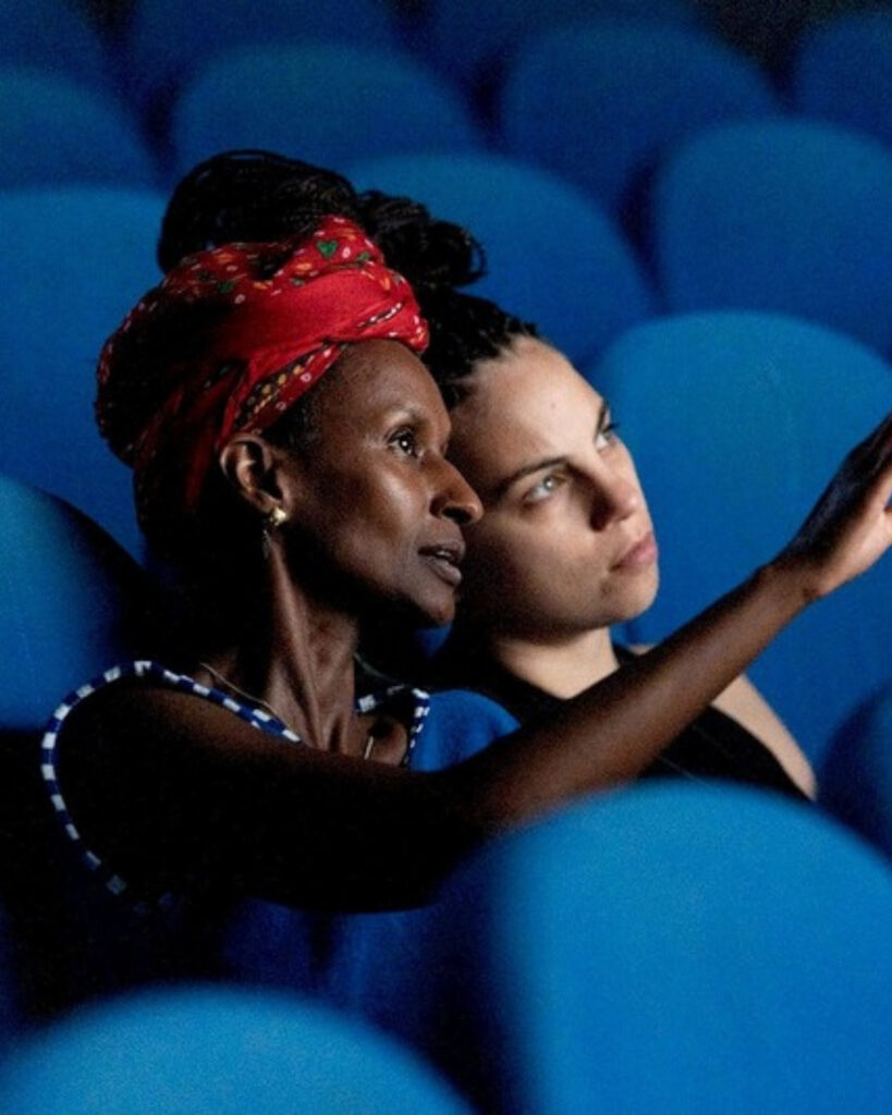 Two women watch from blue theatre seats at Alkantara Festival
